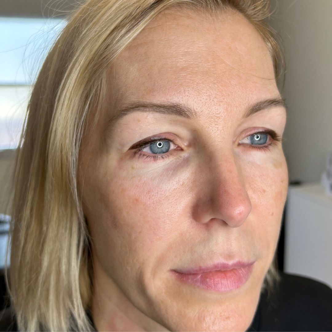 Close-up of blonde woman with a natural winged eyeliner tattoo. The dark pigment hugs her lash line, giving her hooded eyes more shape and definition.