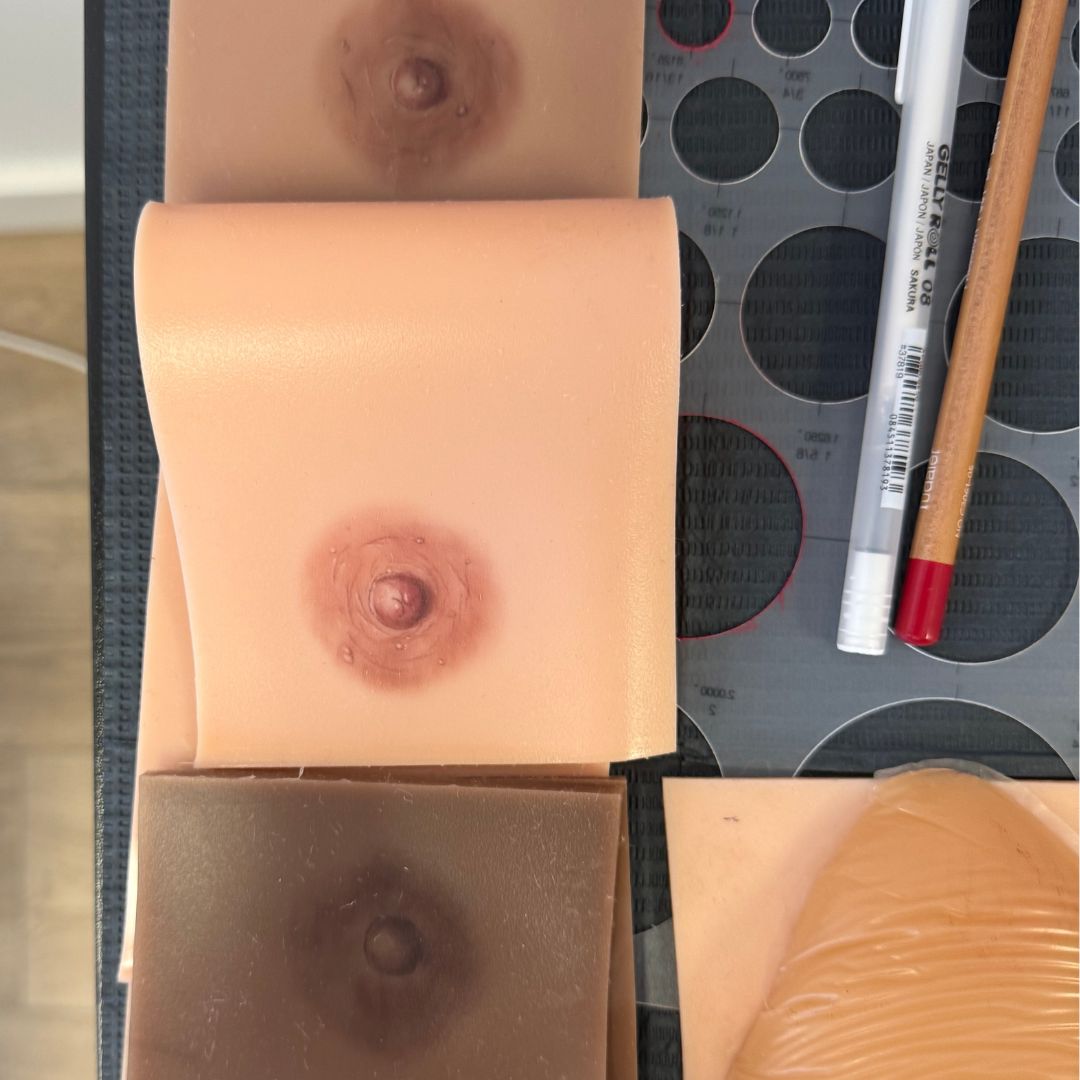 Practice skins with realistic 3D areola and nipple tattoos in different skin tones, used for paramedical tattoo training. The samples show shading, color blending, and texture work that replicate natural areolas, preparing artists to perform nipple tattooing and areola restoration for clients after mastectomy or breast reconstruction.