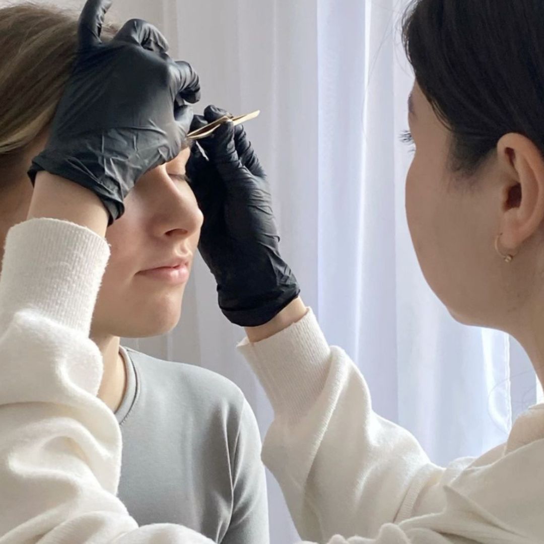 Person getting eyebrow threading from another person with gloves on.