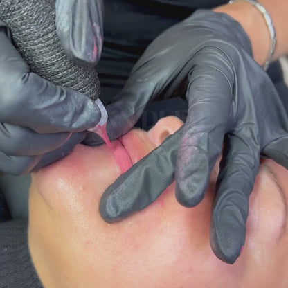 Close-up of a permanent lip blush procedure in Grimsby showing a technician applying soft pink pigment with a tattoo machine to neutralize and enhance natural lip color during treatment.